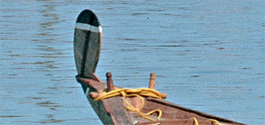 A small craft being poled with a lateen sail and simple painted prow
