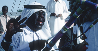 A drummer seen through the strings of a tambura