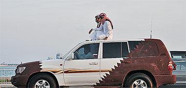 Two Qataris sitting on the roof of their car on National Day